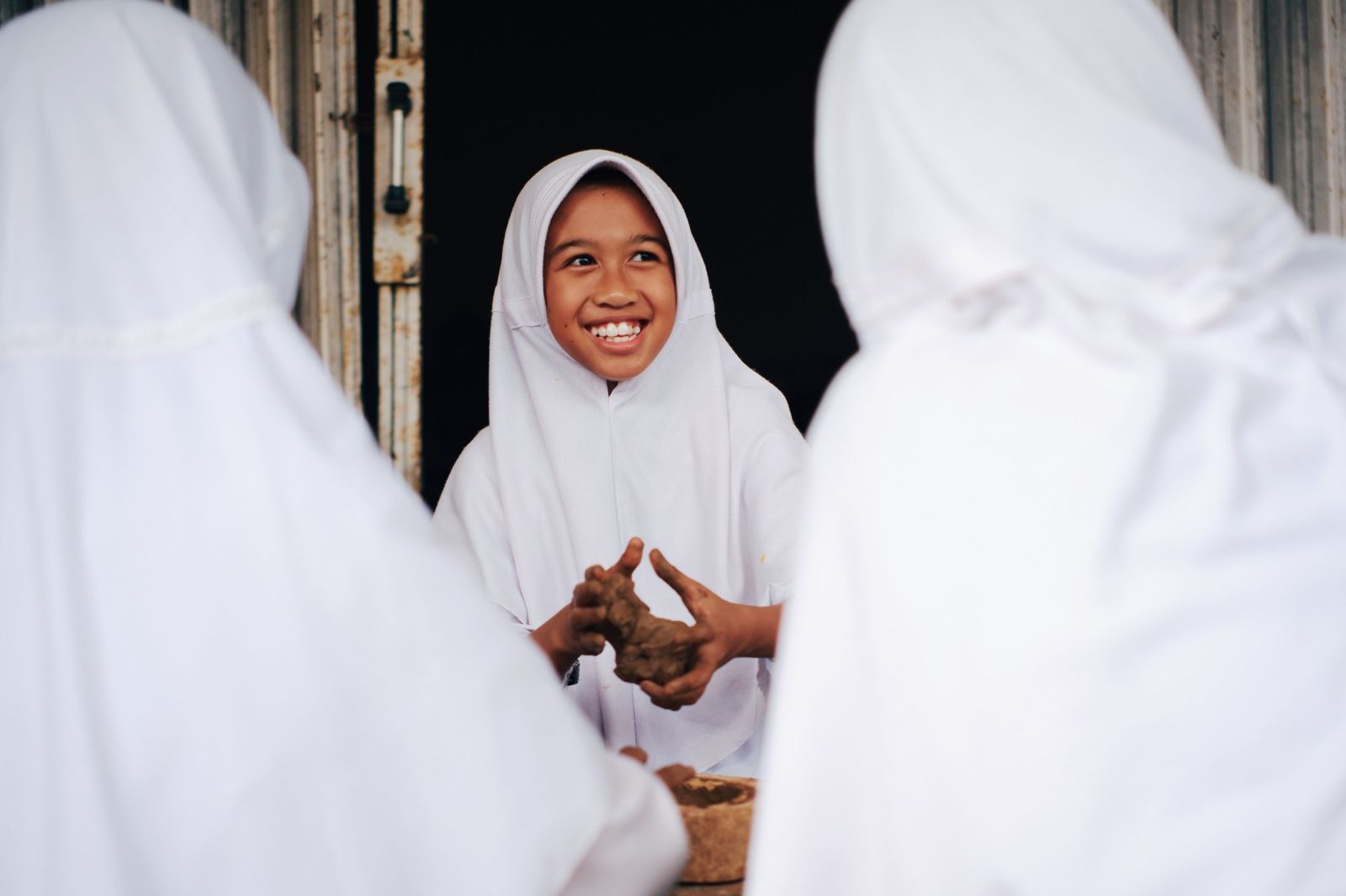 A girl smiling as she shapes clay with classmates